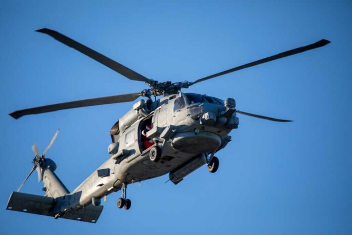 A,U.s.,Navy,Helicopter,Flying,Overhead Silhouette of a helicopter flying over a city skyline at sunset