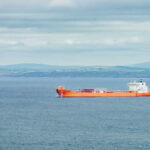 Orange cargo ship sailing on calm sea with distant green hills