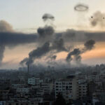 Smoke rising over cityscape at sunset; two birds flying.