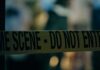 Caution tape marking a crime scene with blurred figures in the background