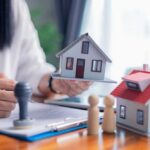Washington Grabs Housing Power—Who Loses? Person holding a model house while signing a document