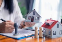 Person holding a model house while signing a document