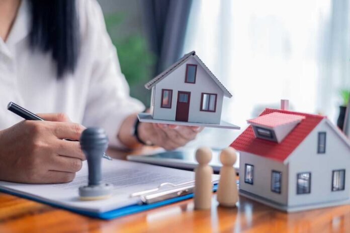 Person holding a model house while signing a document