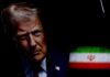 Close-up portrait of a man with a serious expression, with the Iranian flag in the background