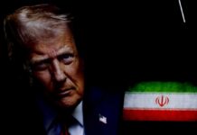 Close-up portrait of a man with a serious expression, with the Iranian flag in the background
