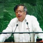 Trump Ally Surges — Defeated President Cries Foreign Hack A speaker in a white shirt addressing an audience at a podium