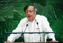 A speaker in a white shirt addressing an audience at a podium