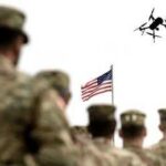soldiers watch a drone fly near an american flag