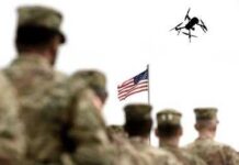 soldiers watch a drone fly near an american flag