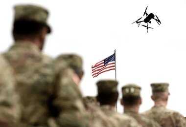 soldiers watch a drone fly near an american flag