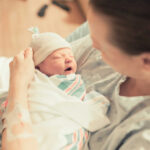 A mother holding her newborn baby in a hospital room, both looking at each other with joy.