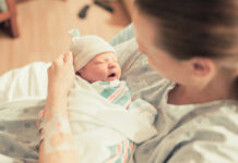America’s Families Are Changing In Unexpected Ways A mother holding her newborn baby in a hospital room, both looking at each other with joy.