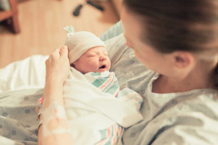 A mother holding her newborn baby in a hospital room, both looking at each other with joy.