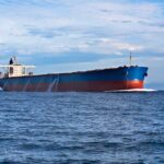 The Hidden Iran Tax At Every Gas Pump A large cargo ship sailing on the ocean under a blue sky