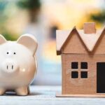 What’s Really Behind Sky-High Home Prices? Piggy bank beside cardboard house model on a table