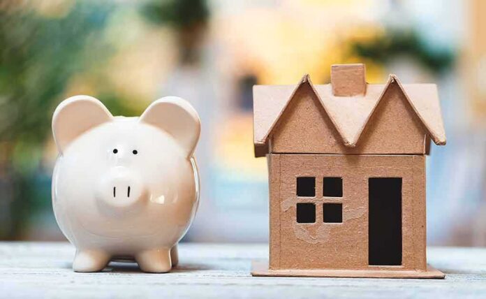 shutterstock_1245931882 Piggy bank beside cardboard house model on a table