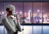 Humanoid robot thinking by window overlooking blurred city skyline