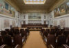 Impeachment Move, Sudden Death — What Happened? Interior view of a courtroom with wooden benches and large murals
