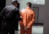 Police officer escorting handcuffed inmate in orange jumpsuit