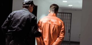 Police officer escorting handcuffed inmate in orange jumpsuit