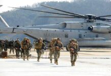 Soldiers disembark and walk past a large military helicopter