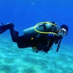 Scuba diver swimming underwater over sandy seabed