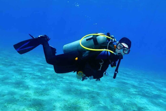 Scuba diver swimming underwater over sandy seabed