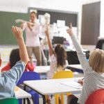 Elementary students raise hands in a classroom