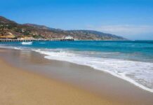 Sandy beach with gentle waves and a long pier by coastal hills