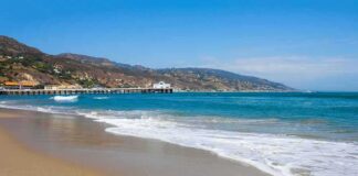 Sandy beach with gentle waves and a long pier by coastal hills