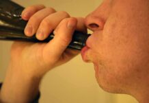 Person drinking from a dark bottle close-up