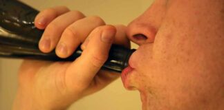Person drinking from a dark bottle close-up