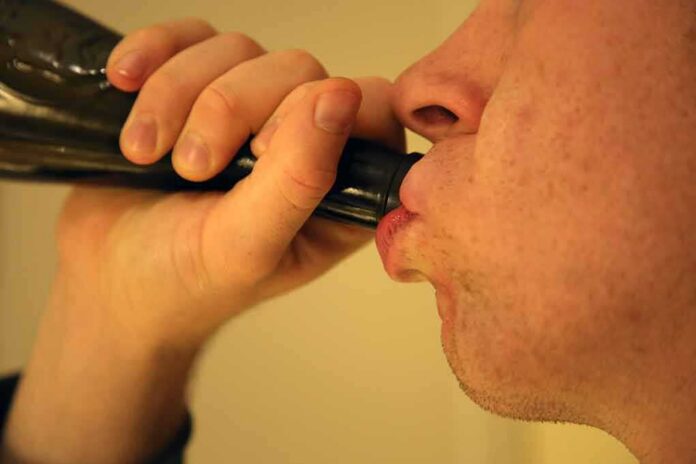 Person drinking from a dark bottle close-up
