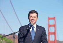 The Electoral College Debate Returns Again man in suit speaking at a microphone near a red suspension bridge