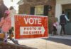 Opposes ID, Now Begs For Trust? Red voting sign with arrow near people entering a polling place