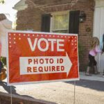 Opposes ID, Now Begs For Trust? Red voting sign with arrow near people entering a polling place