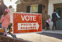 Red voting sign with arrow near people entering a polling place