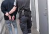 Security officer escorts handcuffed person down hallway