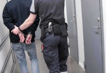Security officer escorts handcuffed person down hallway