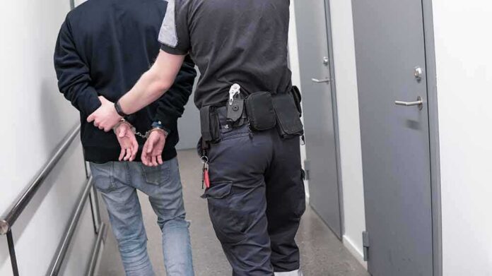 shutterstock_1082126789 Security officer escorts handcuffed person down hallway