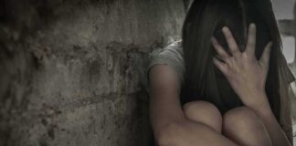 Person sitting against a rough wall with head in hand
