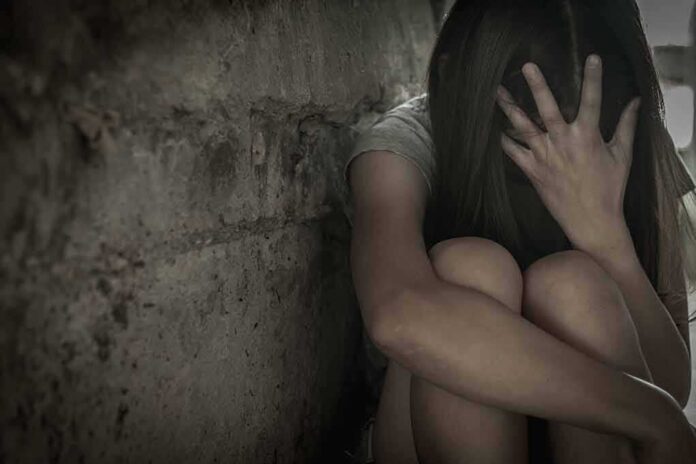 Person sitting against a rough wall with head in hand