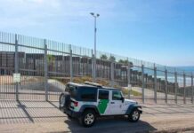 Border patrol SUV parked by tall metal fence near the coast