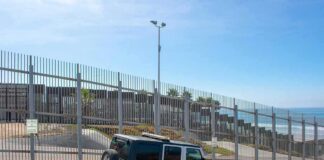 Border patrol SUV parked by tall metal fence near the coast