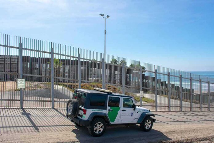 Border patrol SUV parked by tall metal fence near the coast
