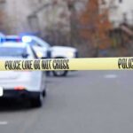 A Federal Shooting Leaves One Crucial Blind Spot Police tape cordons off a street with patrol cars and flashing lights in the background