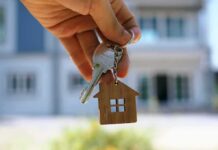 Hand holding house keys with a wooden house keychain