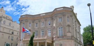 neoclassical stone building with a Cuban flag and iron fence