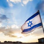 What’s Hidden Behind This Sudden Truce? Israeli flag waving against a sunset backdrop with clouds