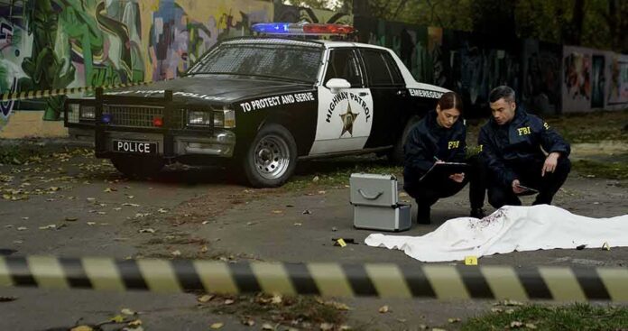 Crime scene with police car and two investigators by a covered body